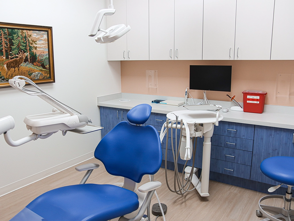 Happy Harbor Pediatric Dentistry operatory with a blue patient chair, cabinetry and a workstation monitor.