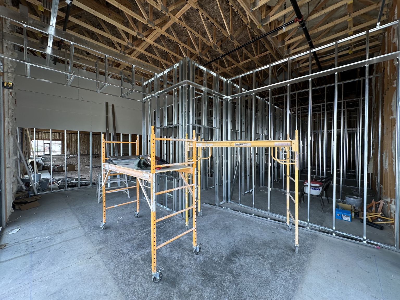 Haven Dental room during construction with exposed roof trusses, metal wall framing and mobile scaffolding.